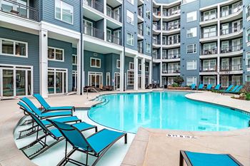 a swimming pool with blue chairs in front of an apartment building